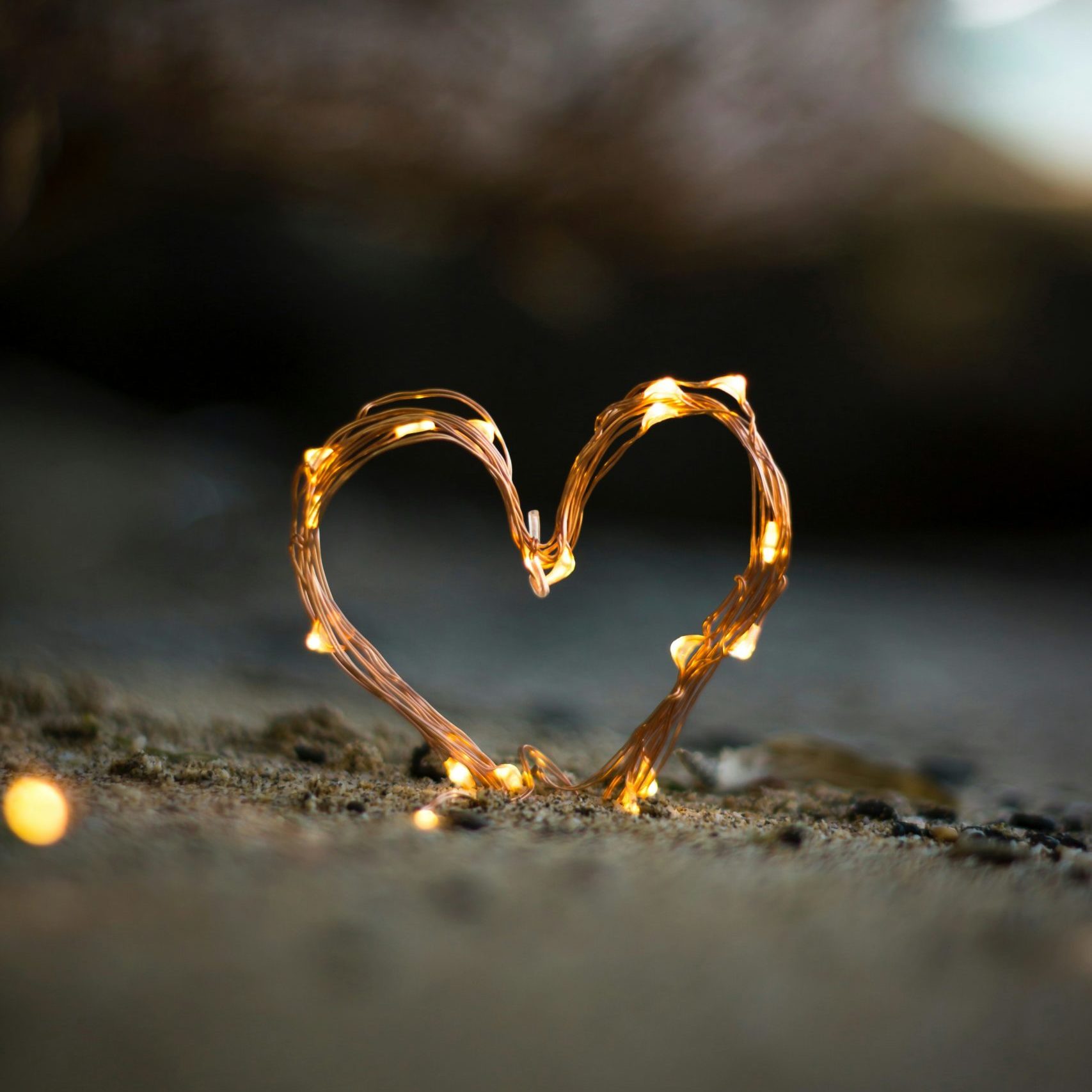 A small heart made of fairy lights set up on a sandy beach