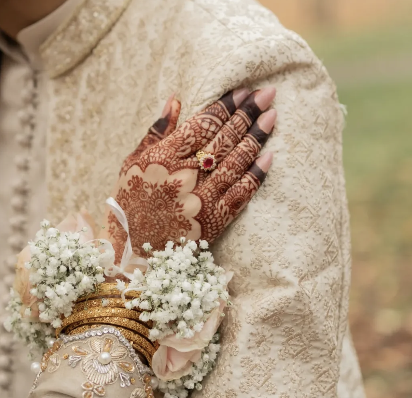 A bride's hand resting on a groom's shoulder decorated with Pakistani henna and a flower garland wrapped around her wrist