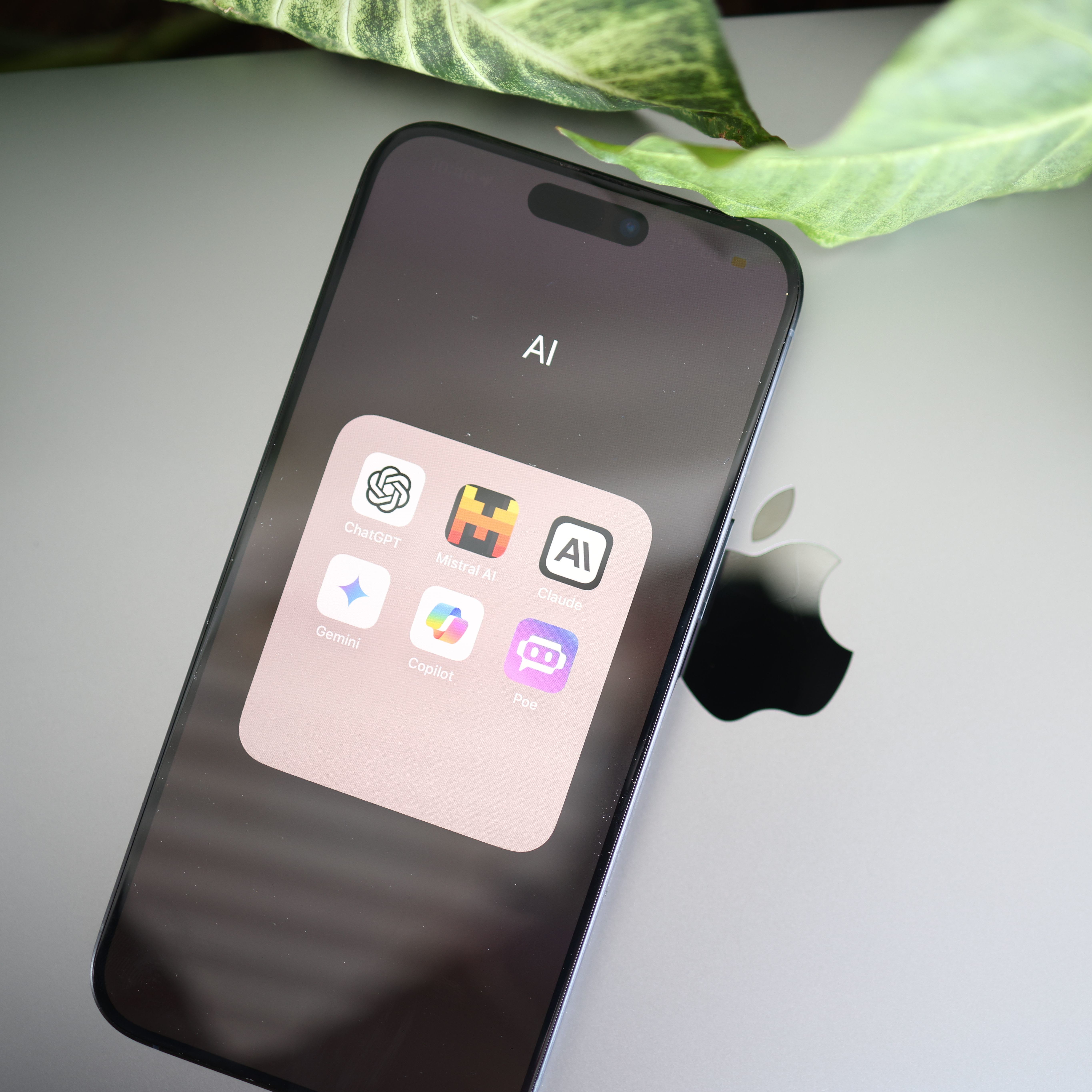 The image shows an Iphone with a folder named AI and includes apps such as ChatGPT, claude, Gemini, Poe and Copilot.