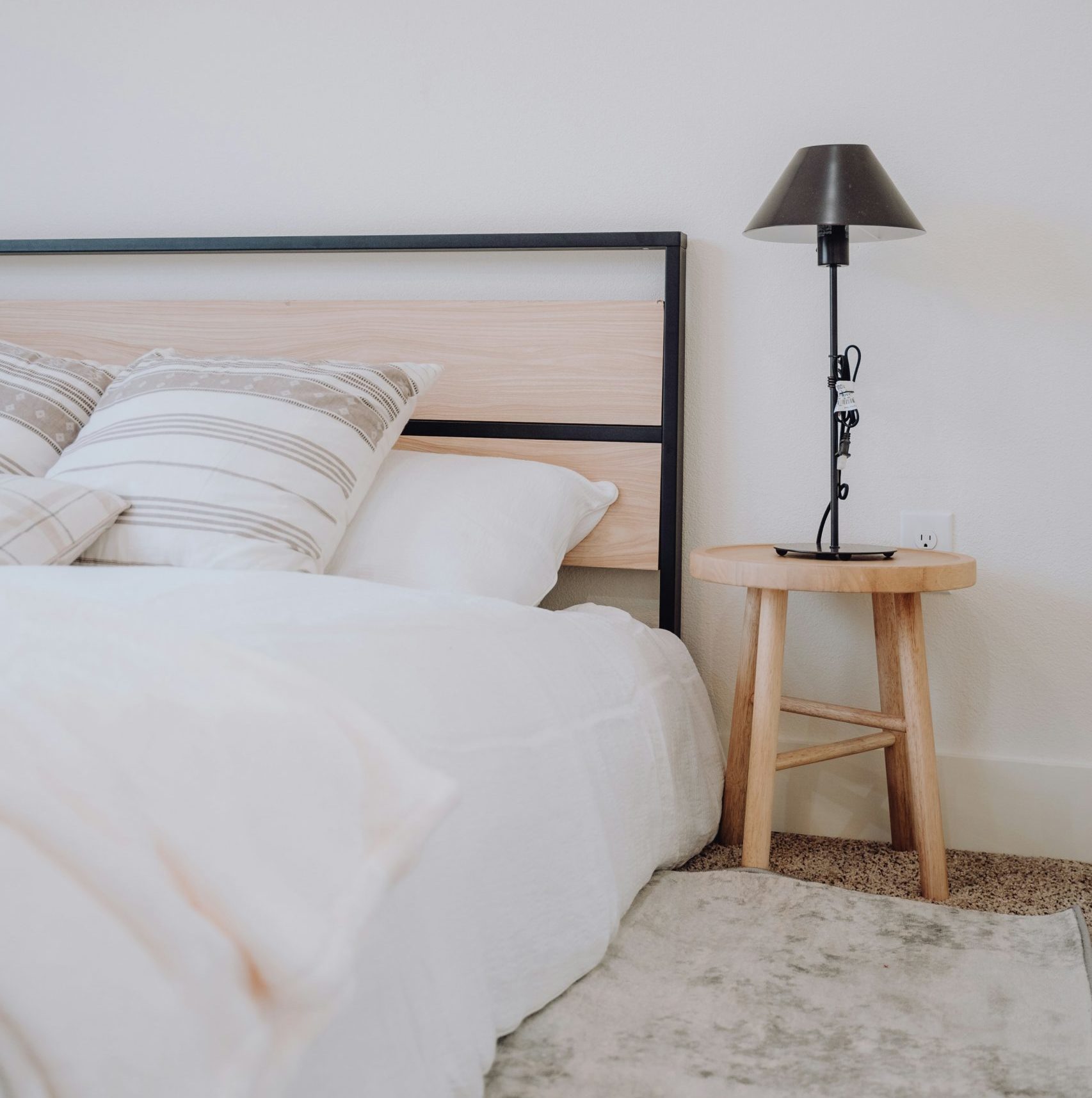 Image showing a view of a bed made with crisp white linens, decorative beige and white cushions, a small three legged side table with a black lamp on top. symbol of marital bed and overcoming religious guilt about sex after nikah
