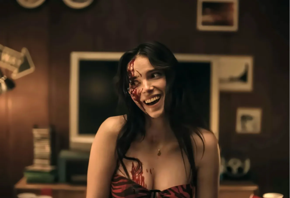 A still from the horror film Obsession showing a white woman with a maniacal and gleeful expression and blood running down the side of her face