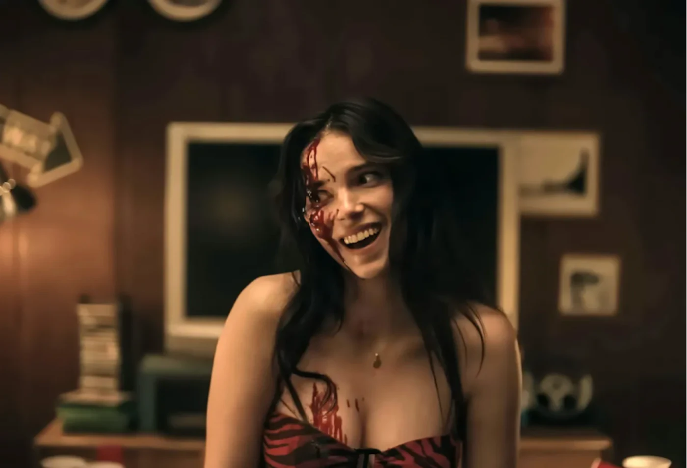 A still from the horror film Obsession showing a white woman with a maniacal and gleeful expression and blood running down the side of her face