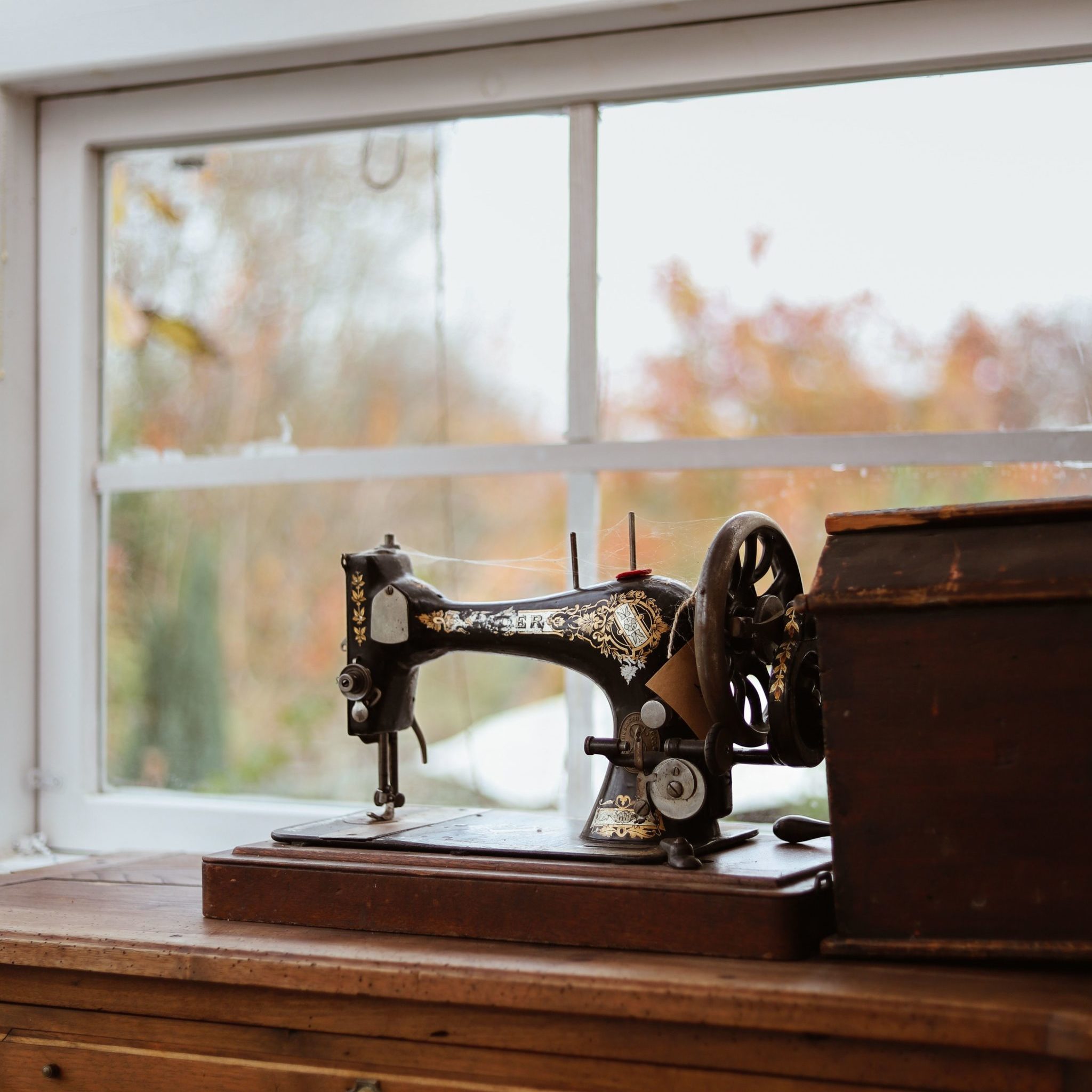 A black singer sewing machine on a brown table in front of a white french panes window