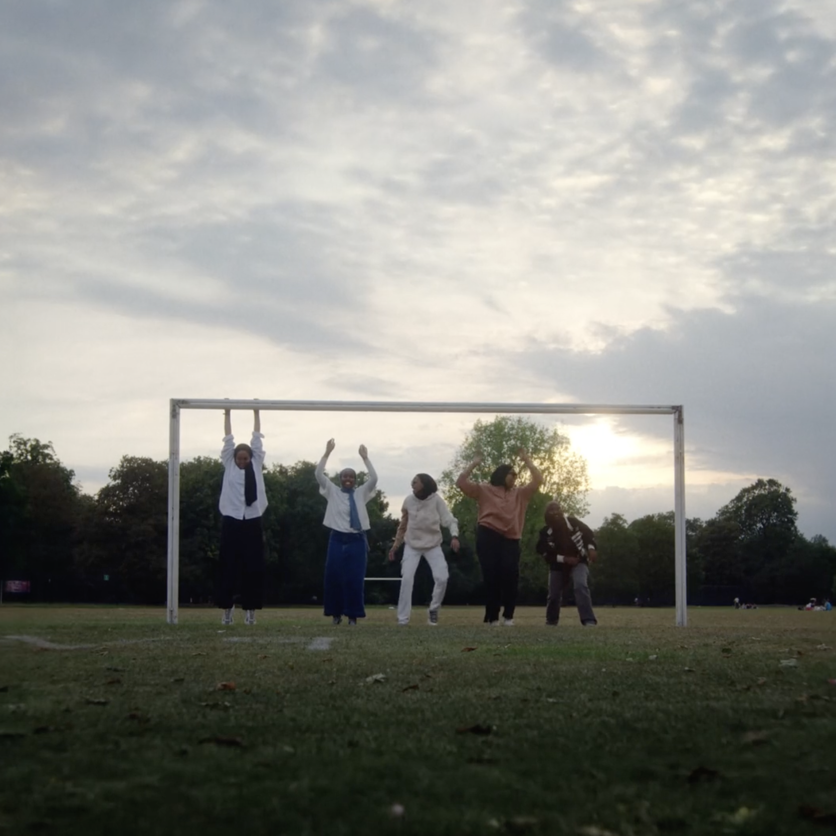 Image shows 5 muslim women standing in front of a goal in a football field and celebrating. A Still from the documentary film Sisterhood FC