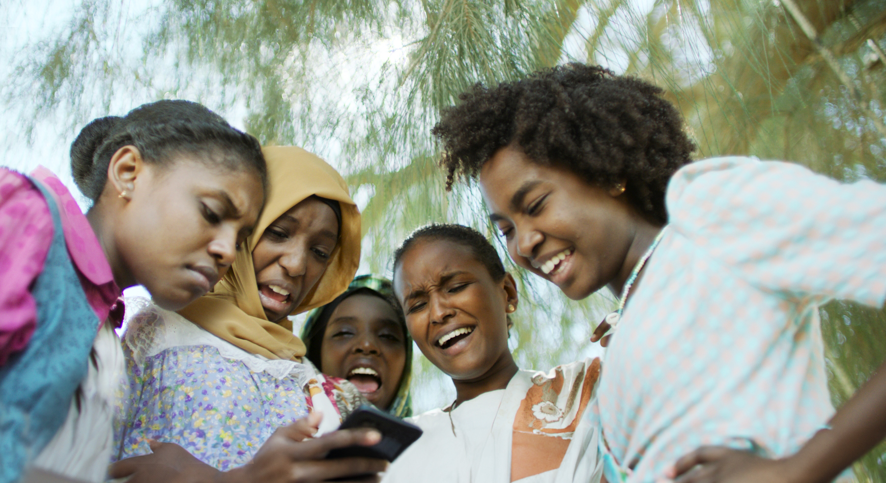 A group of adolescent Sudanese girls looking at a phone together and laughing