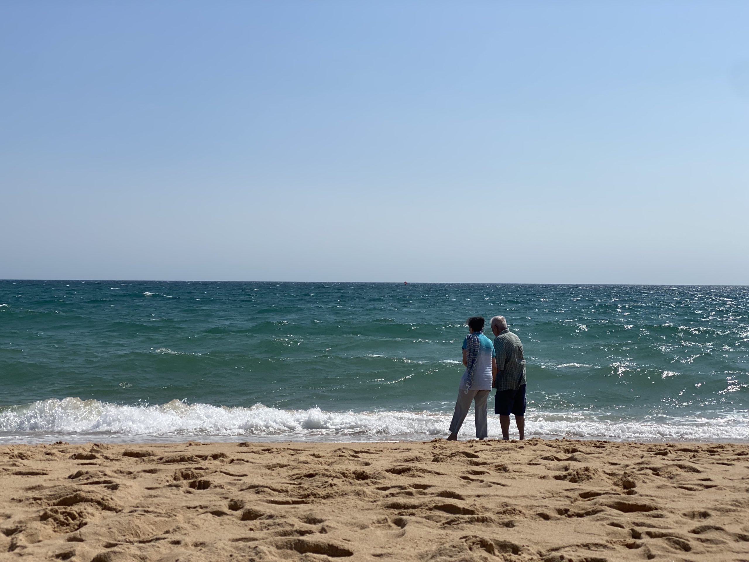 An elderly couple looking out at the ocean, family travel as refugee family
